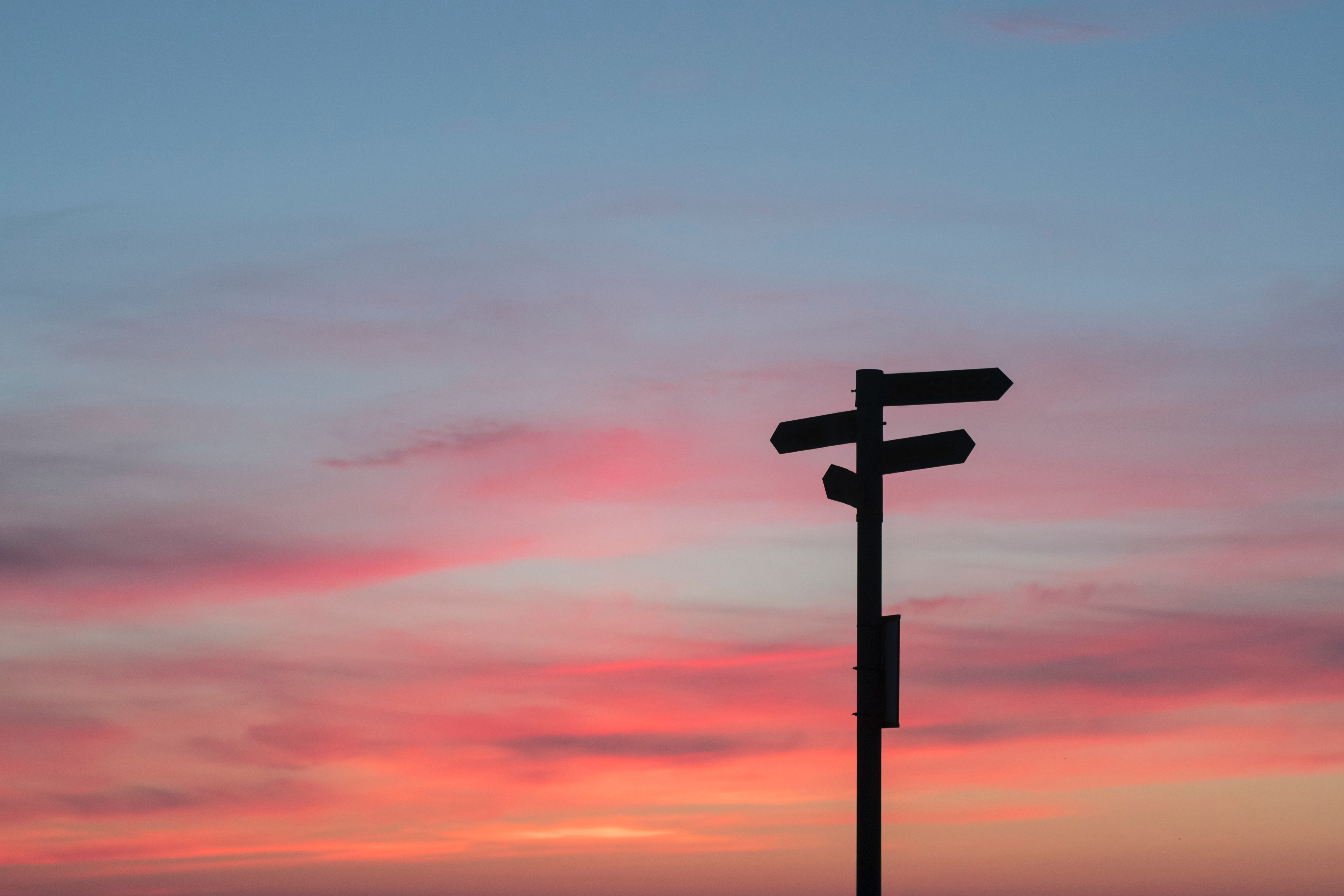 sign posts point in multiple directions silhouetted against the pink, orange and blue sky